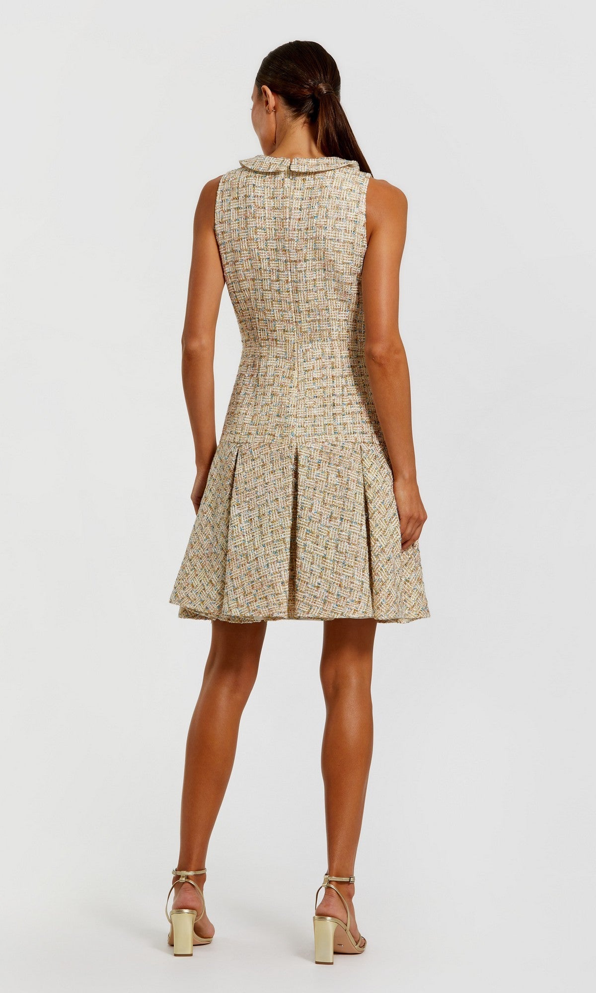 A woman faces away, wearing the Mac Duggal 21068 Short Party Dress with a pleated skirt and beige high-heeled sandals against a plain white background.